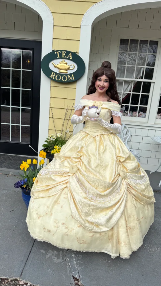 A storybook character in a yellow ball gown standing at the tea room door
