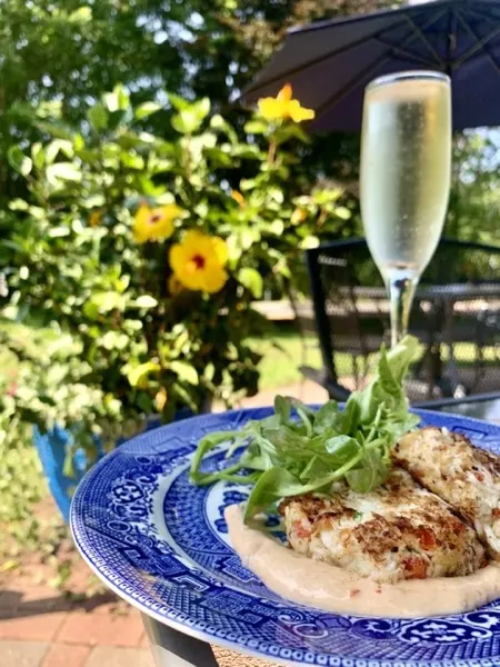 Crab cake with greens on a blue willow plate beside a glass of sparkling wine