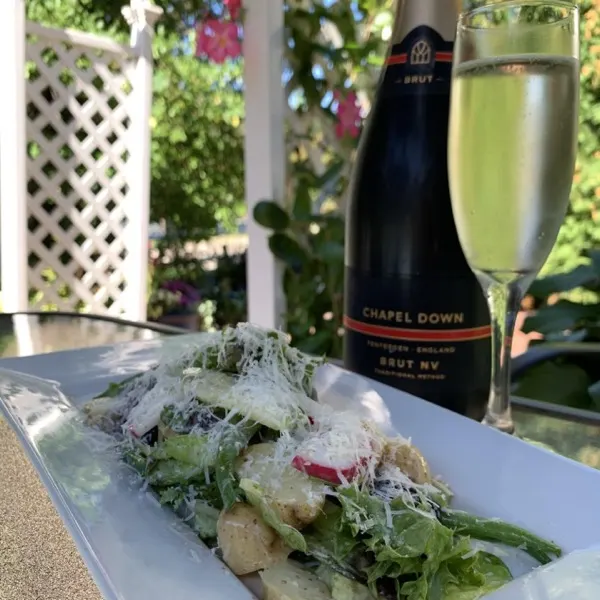 Garden salad with shaved cheese beside a bottle of sparkling wine