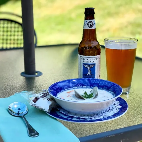 A bowl of clam chowder beside a pale ale on the patio