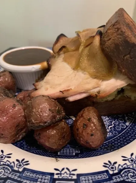 Sliced roast beef with roasted potatoes and a small cup of gravy