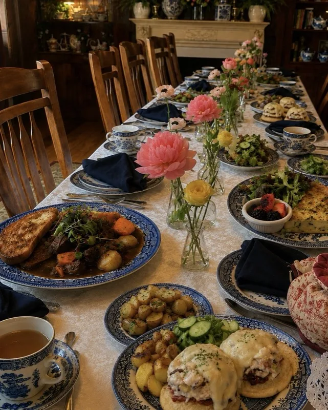 A lunch table set with blue willow plates of roasted potatoes, salad and a pot of tea