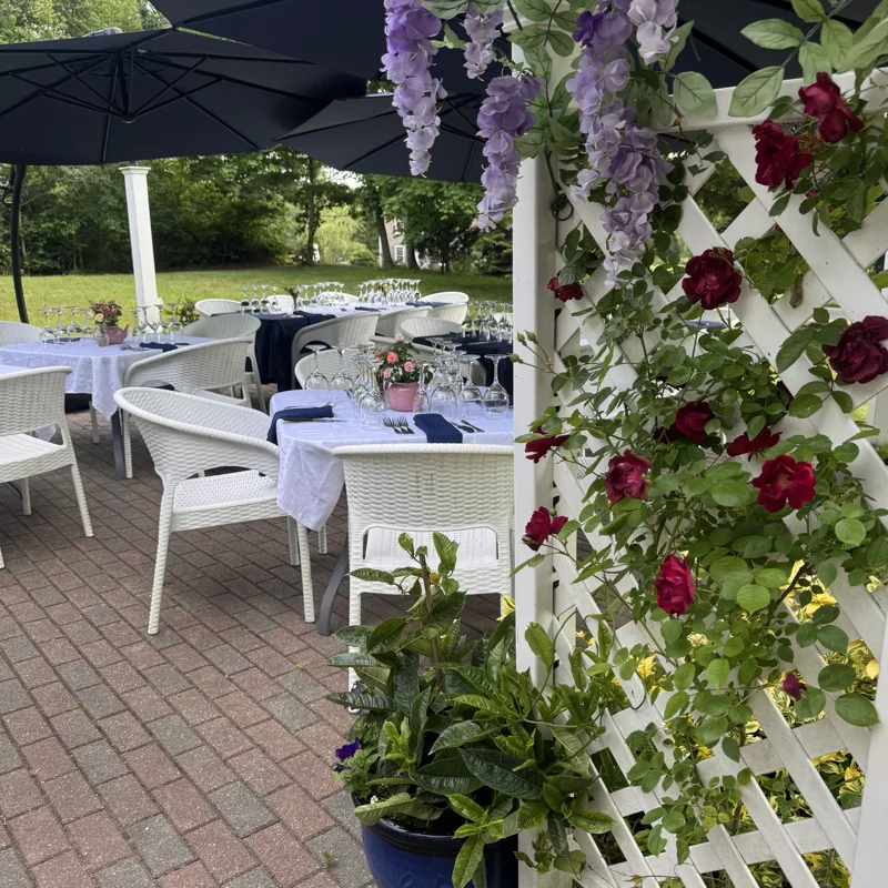 The brick patio with white chairs and a trellis of climbing roses