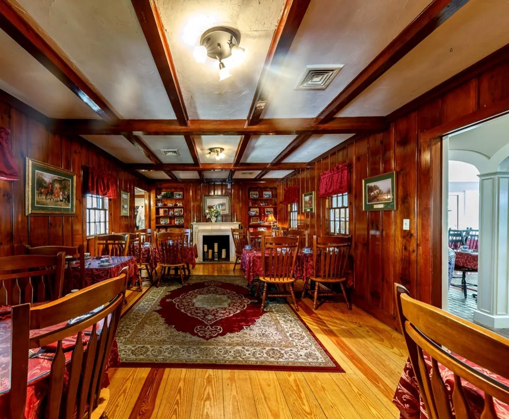The wood-paneled tea room parlor with a fireplace, red rug and set tables